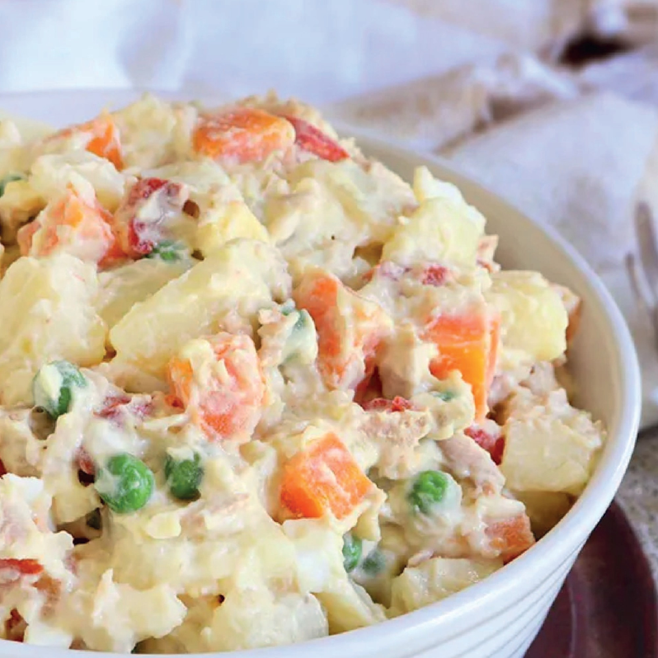 A white bowl filled with creamy Russian salad, featuring potatoes, carrots, and peas.