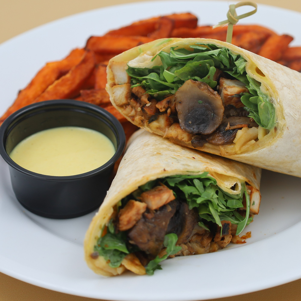 Two halves of a chicken and mushroom wrap with arugula, served with sweet potato fries and dipping sauce.