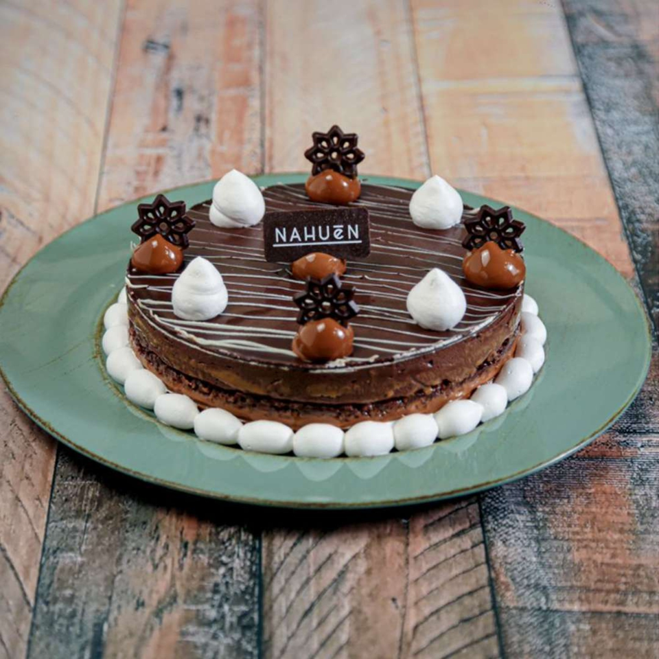 NAHUEN Gourmet Market's chocolate cake with dulce de leche, meringue, and chocolate decorations on a green plate.