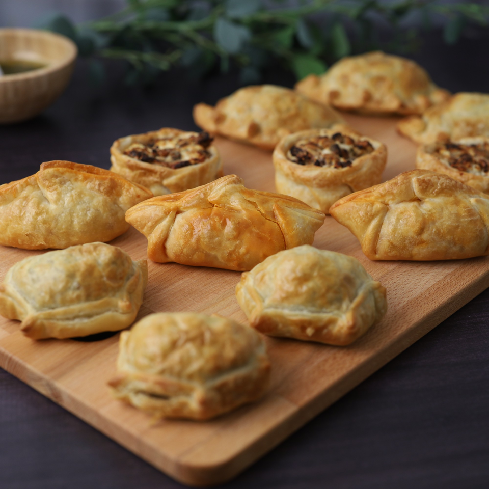 A wooden board filled with golden-brown Argentinian empanadas and savory tarts, ready to eat.