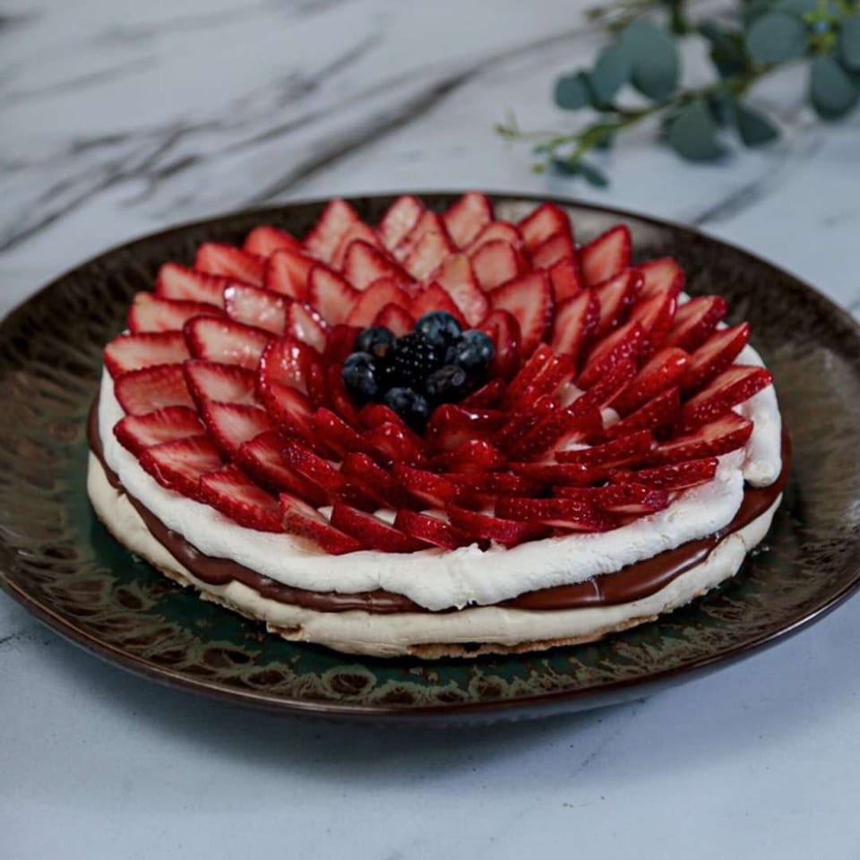 A strawberry and blueberry meringue cake with chocolate filling on a dark plate.