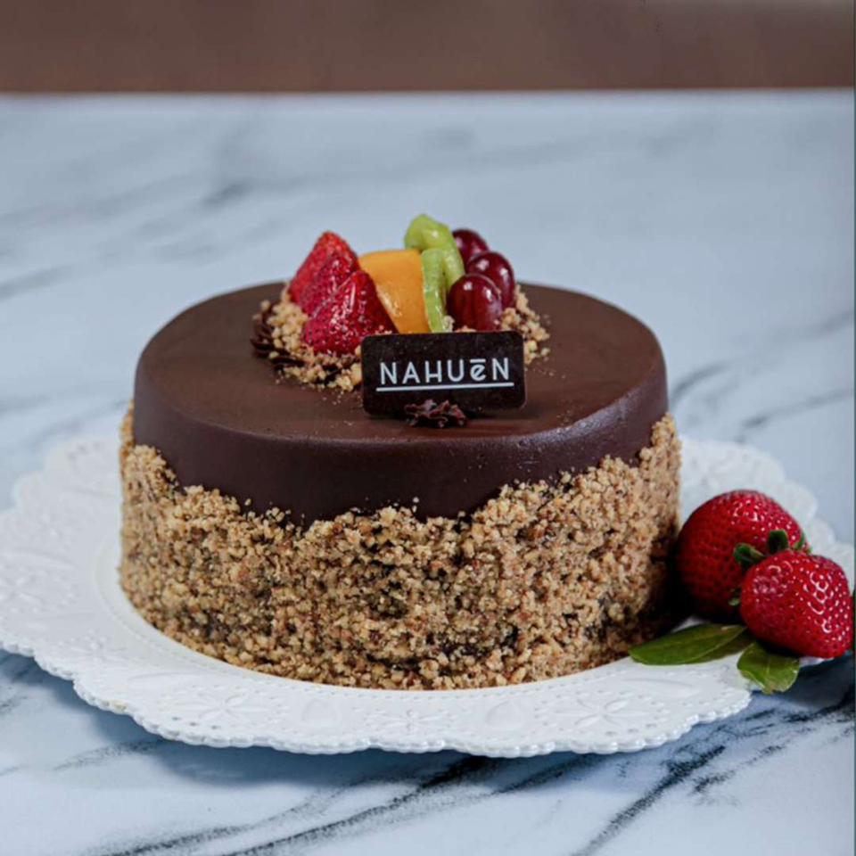 NAHUEN Gourmet Market's chocolate cake with nuts, fresh fruit, and strawberries on a white plate.