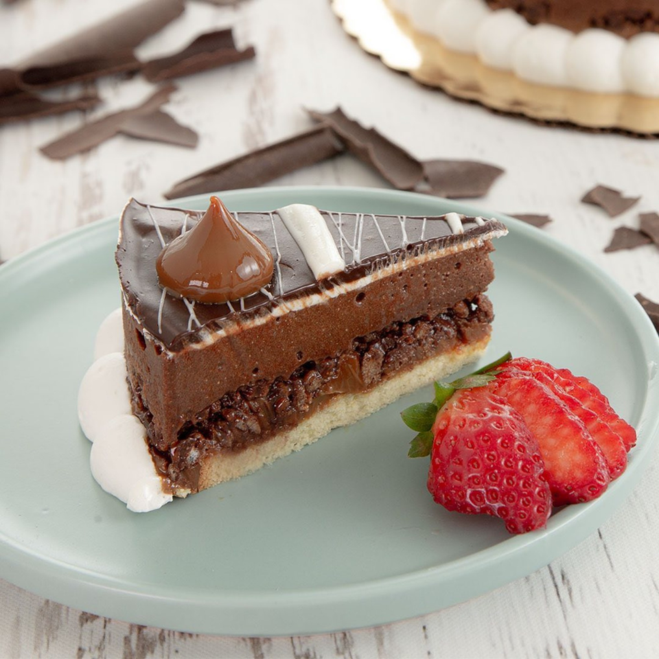 A slice of chocolate cake with dulce de leche, whipped cream, and sliced strawberries on a plate.