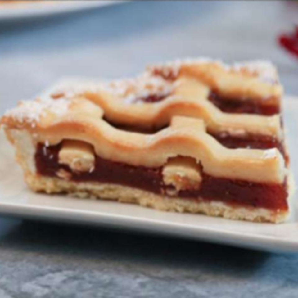 A slice of Argentinian pastafrola, a quince tart with a lattice crust, on a white plate.