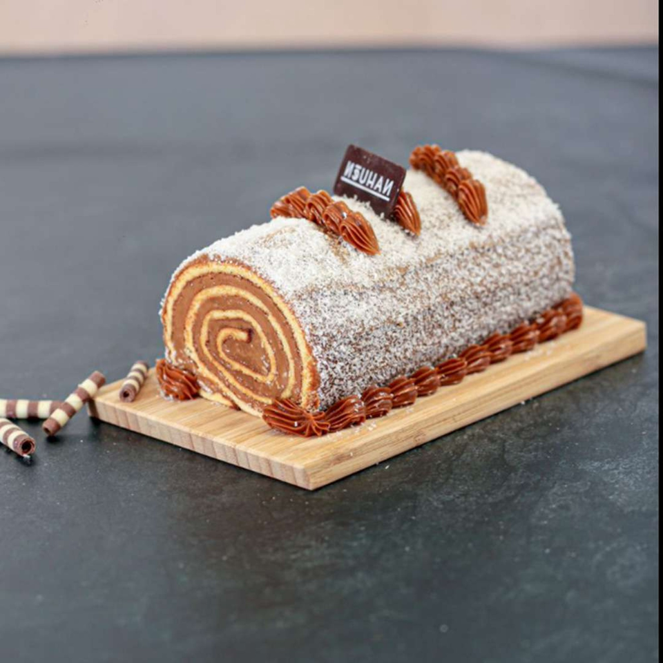 A Nahuen chocolate swiss roll cake, dusted with coconut flakes and dulce de leche frosting.